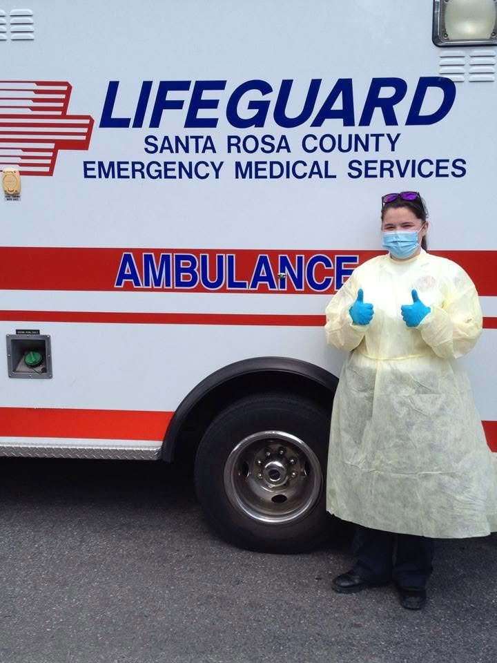 Chelsea in full protective gear giving two thumbs up in front of an ambulance